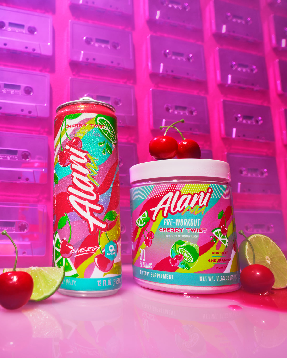 Cherry Twist Energy and Pre-Workout are placed next to each other on a pink floor surrounded by cherries and limes with a wall of cassette tapes in the background. 