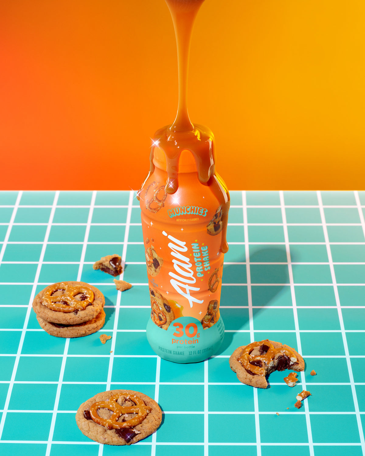 An overhead image of a bottle of Munchies, surrounded by cookies and pretzels as gooey caramel pours over the top. 