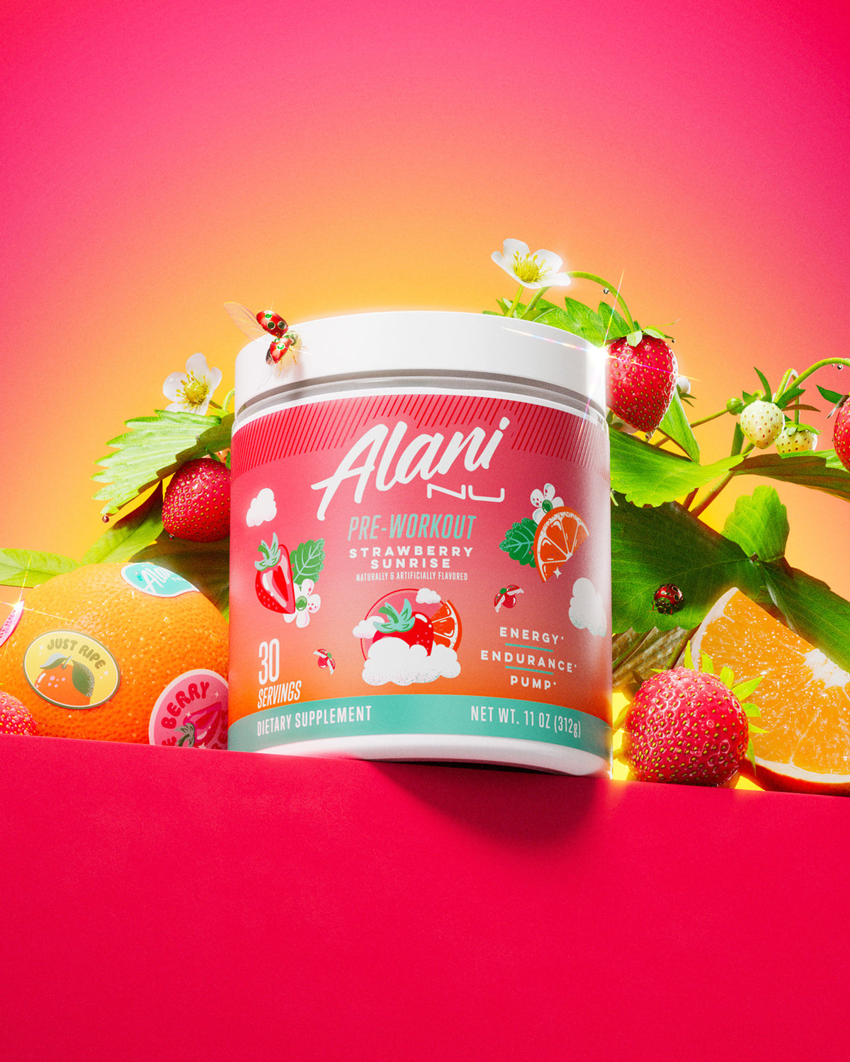 A tub of Alani Nu’s limited-edition Strawberry Sunrise Pre-Workout placed in a pile of bright strawberries and juicy oranges. 