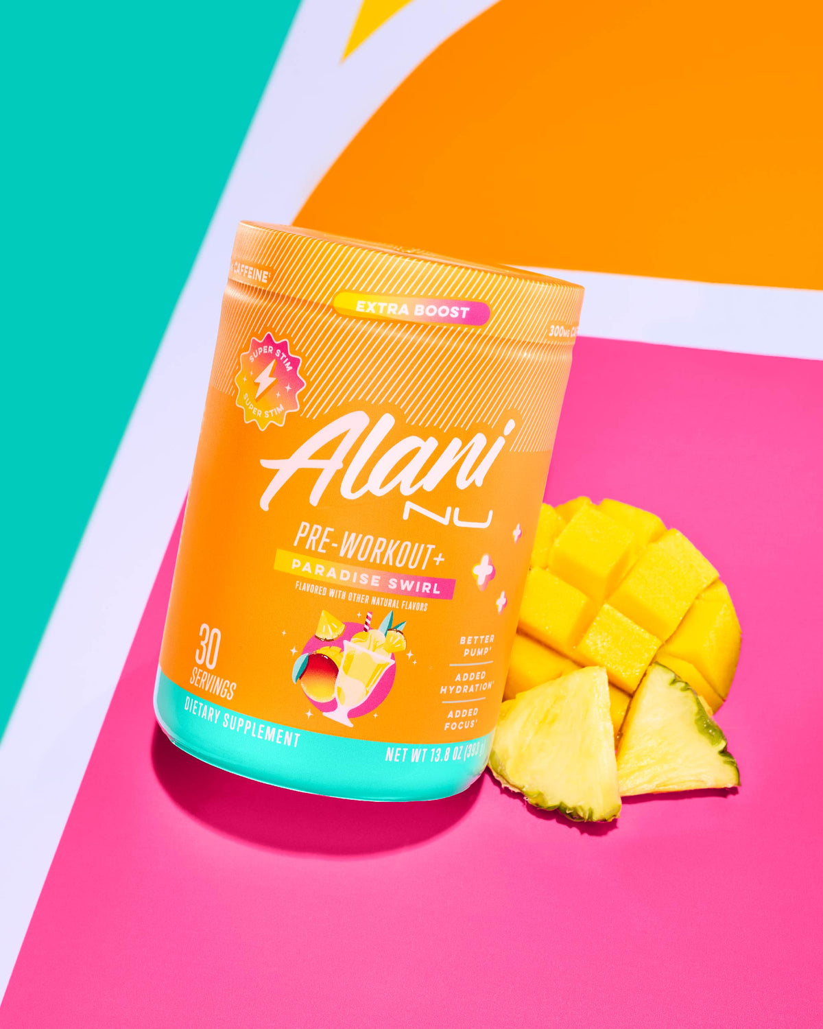 A container of Alani Nu Pre-Workout + - Paradise Swirl is displayed on a colorful background with pineapple and mango slices beside it, available at The Vitamin Shoppe.